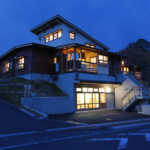 夕暮れ時の建物の全景です。左のスロープを上がり右に入ると玄関です。