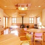 暖炉のあるデイサービスのフロアです。標準より広く取ってあります。食堂は大きな部屋であってもいくつかのコーナーができるように考えてあります。食堂から続くデッキテラスへは車椅子のままでも出ることができます。